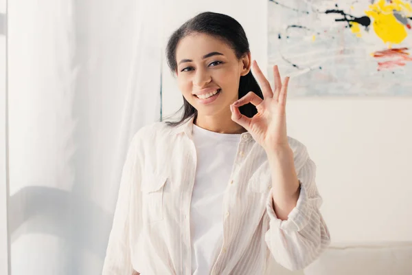 Cheerful latin woman showing ok gesture while smiling at camera — Stock Photo