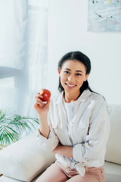 Pretty latin woman holding ripe apple and smiling at camera — Stock Photo