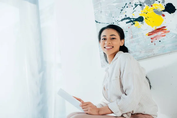 Belle femme latine souriant à la caméra tout en utilisant une tablette numérique à la maison — Photo de stock