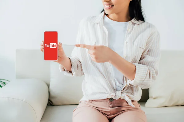 KYIV, UKRAINE - APRIL 26, 2019: Partial view of latin woman pointing with finger at smartphone with Youtube app on screen. — Stock Photo