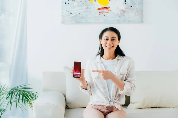 Atractiva mujer latina señalando con el dedo en el teléfono inteligente con cursos de comercio aplicación en la pantalla - foto de stock