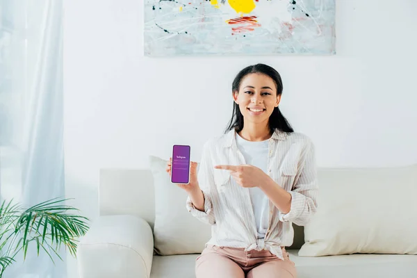 KYIV, UKRAINE - APRIL 26, 2019: Attractive latin woman pointing with finger at smartphone with Instagram app on screen. — Stock Photo