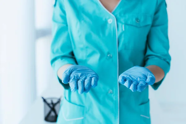 Partial view of nurse in blue uniform and latex gloves holding open palms — Stock Photo