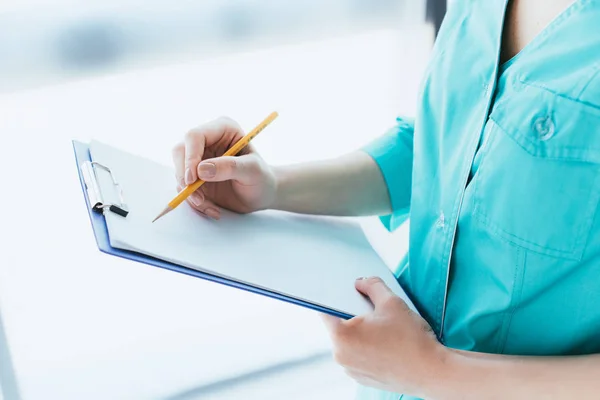 Cropped shot of doctor in blue uniform writing on clipboard — Stock Photo