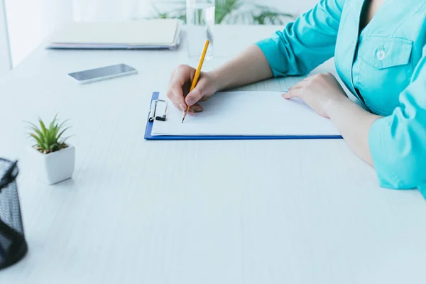 Schnappschuss eines jungen Arztes, der am Arbeitsplatz sitzt und auf Klemmbrett schreibt — Stockfoto