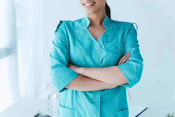 Partial view of young latin doctor standing with crossed arms near workplace — Stock Photo
