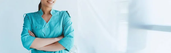 Colpo panoramico di giovane infermiera latina in uniforme blu in piedi con le braccia incrociate — Foto stock
