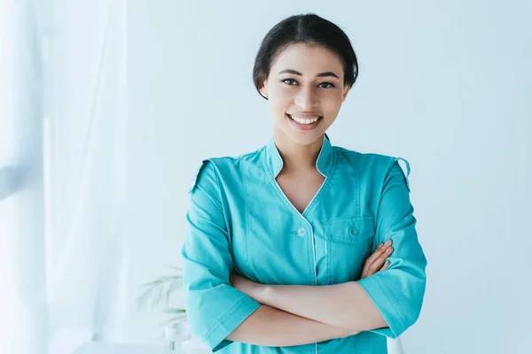 Pretty latin doctor smiling at camera while standing with crossed arms — Stock Photo