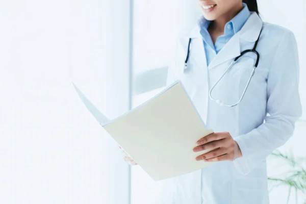 Cropped shot of young latin doctor looking in paper folder while standing by window in hospital — Stock Photo