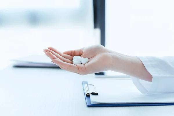 Recortado inyección de médico con un puñado de pastillas cerca de portapapeles en la mesa - foto de stock