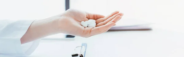 Panoramic shot of cropped shot of doctor with handful of pills near clipboard on table — Stock Photo
