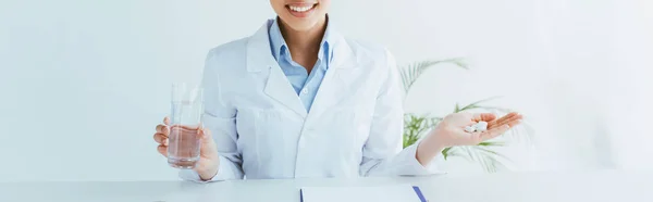 Plan panoramique de médecin souriant avec une poignée de pilules et un verre d'eau — Photo de stock