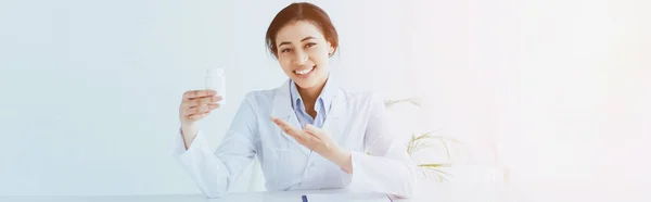 Plan panoramique de sourire médecin latin pointant avec la main au récipient avec des pilules — Photo de stock