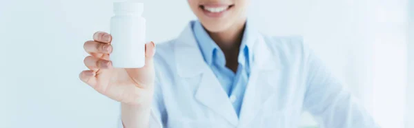 Plano panorámico de sonriente médico latino mostrando contenedor con pastillas - foto de stock