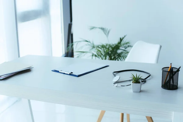 Presse-papiers avec papier blanc, stéthoscope et plante verte en pot sur le bureau de l'hôpital — Photo de stock