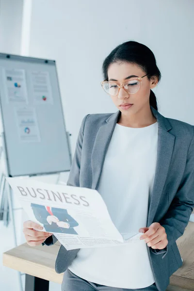 Attentive latin businesswoman in glasses reading business newspaper in office — Stock Photo