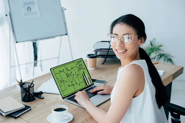 Mulher de negócios latina alegre jogando jogo de futebol online no laptop e olhando para a câmera — Fotografia de Stock