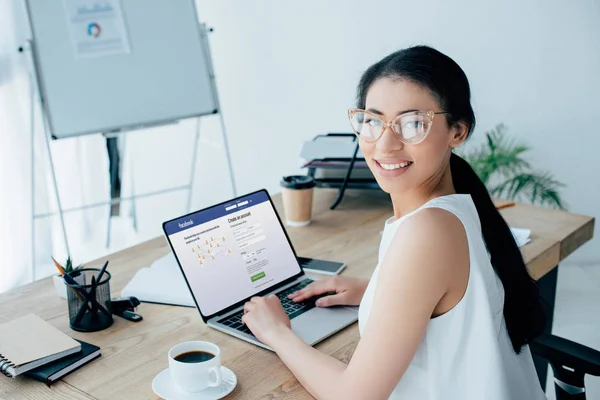 KYIV, UKRAINE - 26 de abril de 2019: Mulher de negócios latina bonita sorrindo para a câmera ao usar o laptop com código html na tela . — Fotografia de Stock