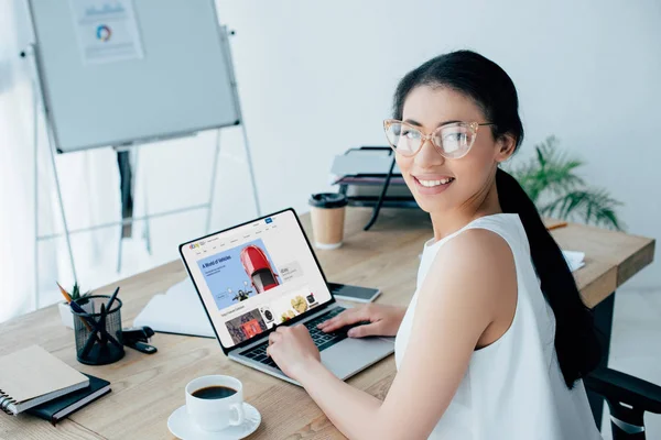 KYIV, UKRAINE - APRIL 26, 2019: Atrractive latin businesswoman smiling at camera while using laptop with Ebay website on screen. — Stock Photo