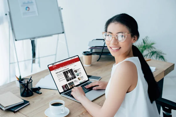 KYIV, UKRAINE - APRIL 26, 2019: Smiling latin businesswoman looking at camera while using laptop with BBC news website on screen. — Stock Photo