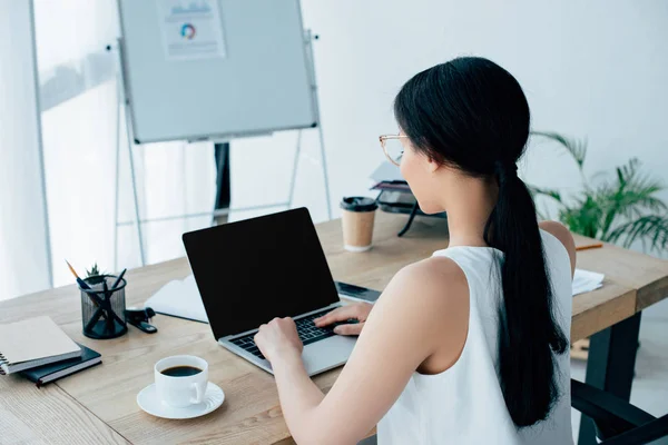 Jeune femme d'affaires latine en utilisant un ordinateur portable tout en étant assis sur le lieu de travail près de tasse de café — Photo de stock