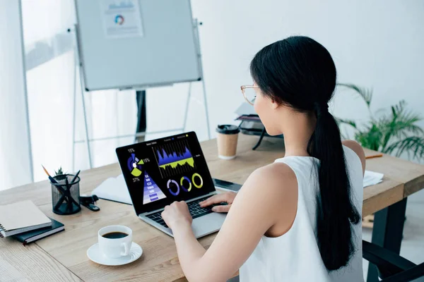 Joven mujer de negocios latina usando portátil con gráficos y gráficos en la pantalla cerca de la taza de café - foto de stock