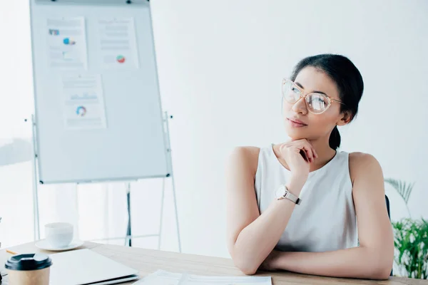 Dreamy latin businesswoman in glasses looking away while sitting at workplace — Stock Photo