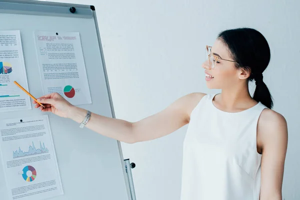 Hübsche Geschäftsfrau zeigt mit Bleistift auf Flipchart mit Infografik — Stockfoto