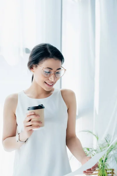 Bonita mujer de negocios latina mirando el papel mientras sostiene la taza desechable - foto de stock