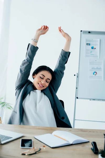 Exhausted latin businesswoman stretching with closed eyes while sitting at workplace — Stock Photo