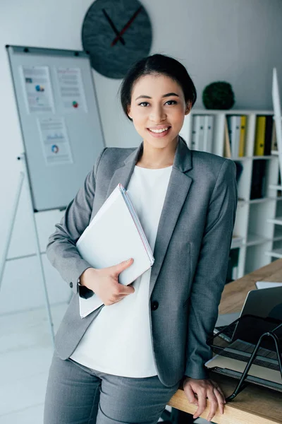 Beautiful latin businesswoman smiling at camera while holding paper folder — Stock Photo