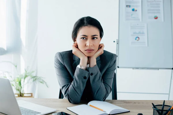 Засмучена латинська бізнес-леді, дивлячись далеко, сидячи на робочому місці в офісі — стокове фото