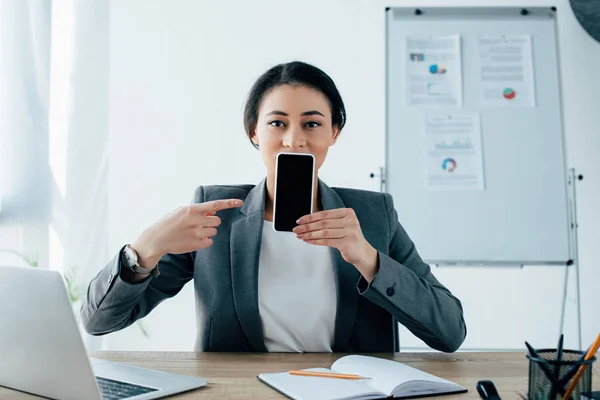 Jeune femme d'affaires latine pointant du doigt le smartphone avec écran vierge — Photo de stock