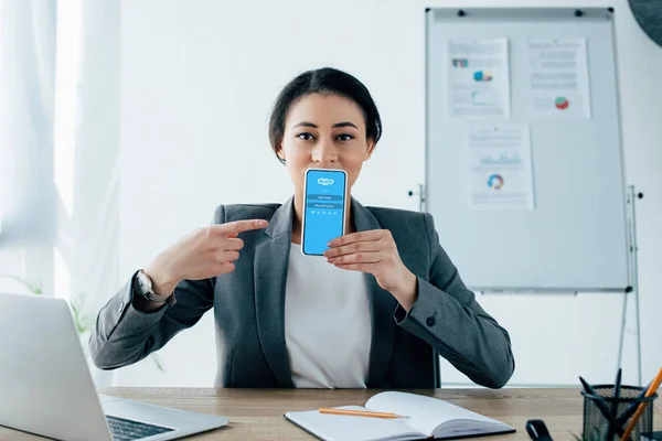 KYIV, UKRAINE - 26 AVRIL 2019 : Une jeune femme d'affaires latine montre son smartphone avec une application Skype à l'écran . — Photo de stock