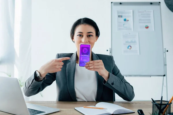 Jovem empresária latina apontando com o dedo para o smartphone com aplicativo de compras na tela — Fotografia de Stock