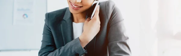 Панорамный снимок улыбающейся латинской деловой женщины, разговаривающей на смартфоне — стоковое фото