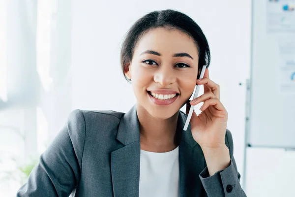 Bela empresária latina sorrindo para a câmera enquanto conversa no smartphone no escritório — Fotografia de Stock
