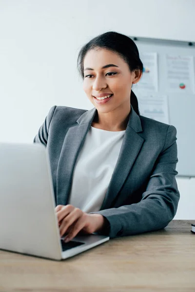 Jolie femme d'affaires latine souriant tout en utilisant un ordinateur portable au bureau — Photo de stock