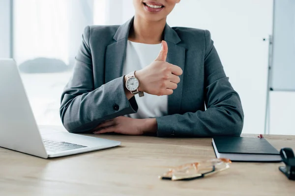 Vista parcial de la mujer de negocios latina mostrando el pulgar hacia arriba mientras está sentada en el lugar de trabajo - foto de stock