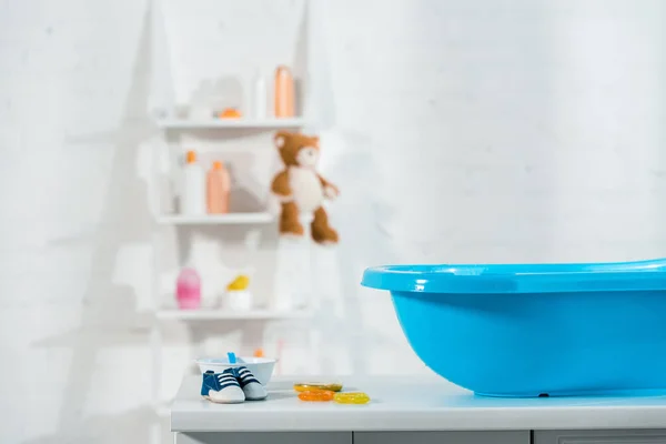 Blaue Babywanne in der Nähe von Babyturnschuhen und Spielzeug im Badezimmer — Stockfoto