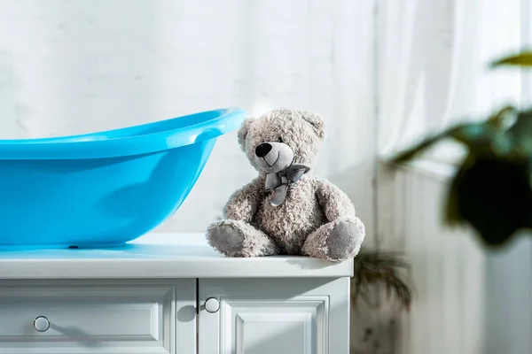 Selective focus of teddy bear near blue baby bathtub in bathroom — Stock Photo