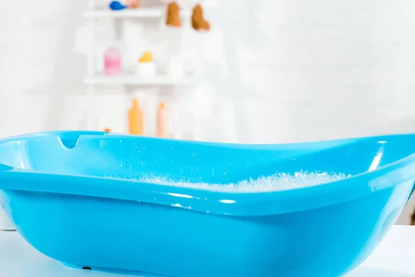 Blue baby bathtub with water and bath foam in bathroom — Stock Photo
