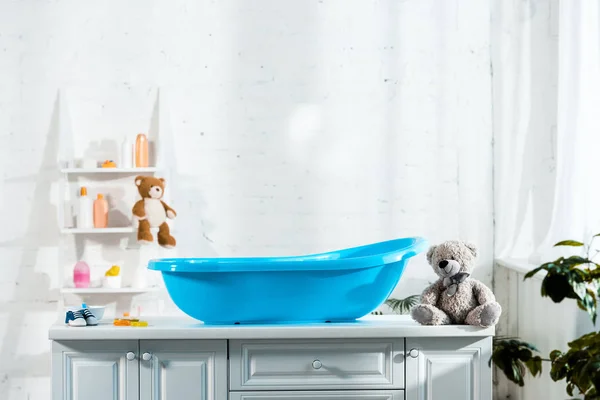 Blaue Babywanne neben Teddybär und Baby-Turnschuhen im Badezimmer — Stockfoto