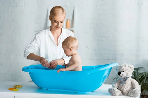 Happy mother looking at cute toddler son taking bath at home — Stock Photo