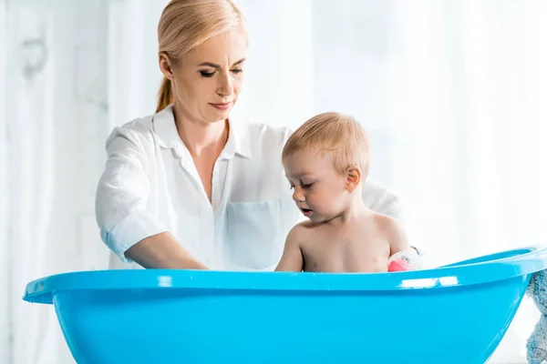 Vista de ángulo bajo de niño lindo tomando baño cerca de la madre en casa - foto de stock