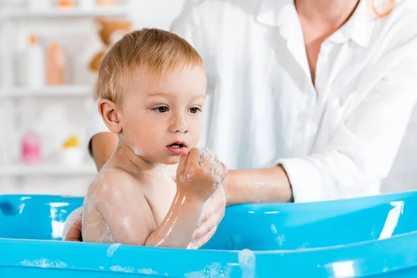 Cropped view of mother washing cute toddler kid in baby bathtub — Stock Photo