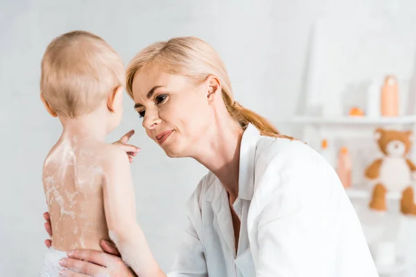 Приваблива блондинка мати дивиться на маленького сина, вказуючи пальцем у ванній кімнаті — стокове фото