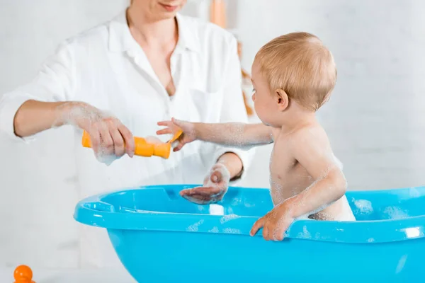 Обрізаний вид матері, що тримає пляшку шампуню біля сина малюка — стокове фото