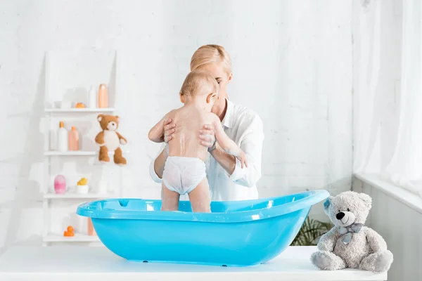 Блондинка мати тримає в руках малюка у ванній кімнаті — стокове фото