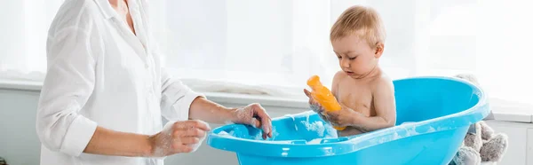 Plan panoramique de la mère près de mignon tout-petit fils tenant bouteille avec shampooing — Photo de stock